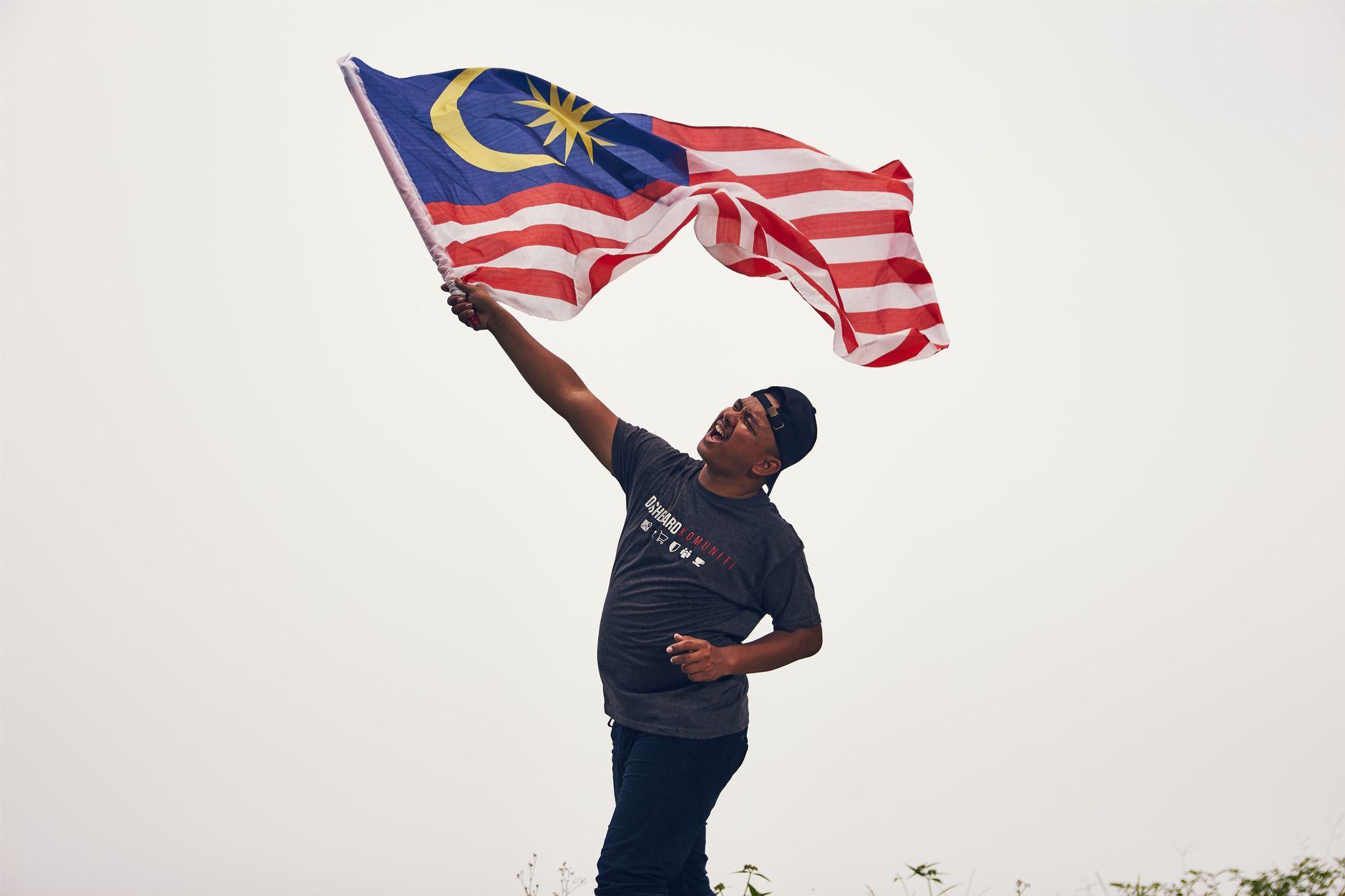 A man proudly waves the Malaysian flag outdoors, expressing joy and patriotism.