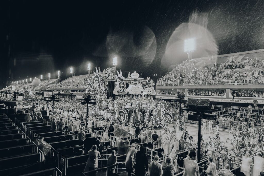 Black and white image of a vibrant parade at the Rio Carnival in the Sambadrome amidst rain.