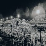 Black and white image of a vibrant parade at the Rio Carnival in the Sambadrome amidst rain.