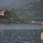 A serene view of a golden statue on Lake Como with lush greenery in the background.