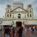 Stunning view of Quiapo Church, Manila, with visitors and a backdrop of skyscrapers.