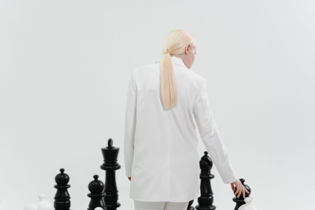 A fashionable woman in white plays a large-scale chess game, symbolizing strategy and intellect.