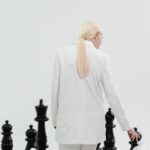 A fashionable woman in white plays a large-scale chess game, symbolizing strategy and intellect.
