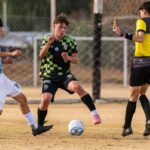 Soccer players in action during a competitive match with referee interaction.