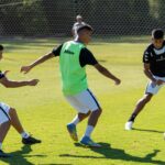 Three young men engage in soccer practice outdoors on a sunny day.