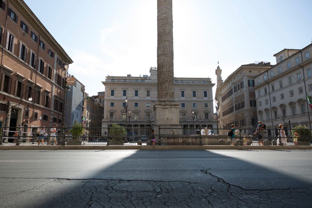 A vibrant daytime scene of an ancient column in a Rome city square with tourists and historic architecture.