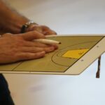 Close-up of a coach using a basketball tactics board to plan game strategy indoors.