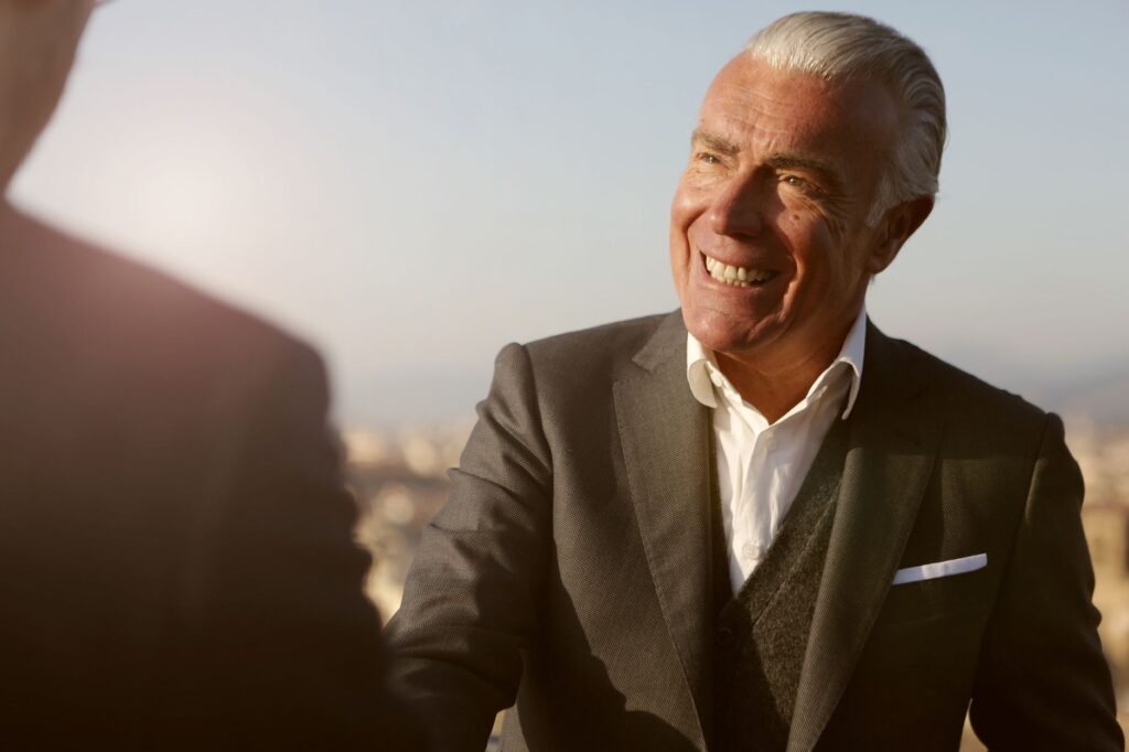 Elderly businessman smiling during a handshake outdoors. Warm, professional and engaging atmosphere.