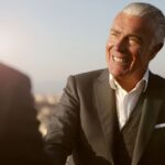 Elderly businessman smiling during a handshake outdoors. Warm, professional and engaging atmosphere.