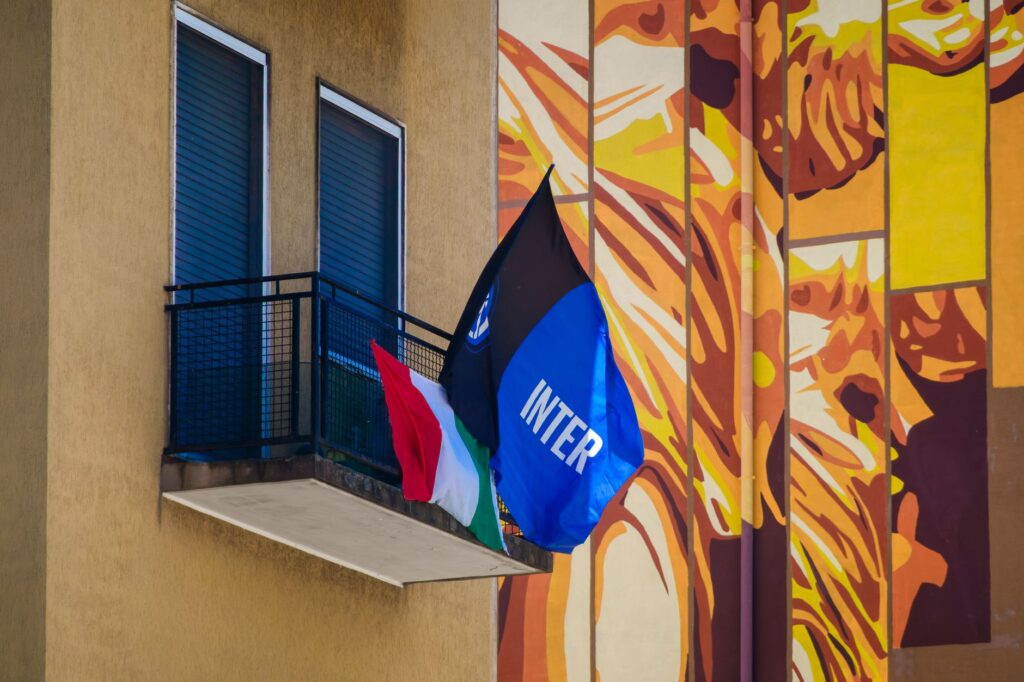 A vibrant urban balcony with flags against a mural backdrop in daylight.