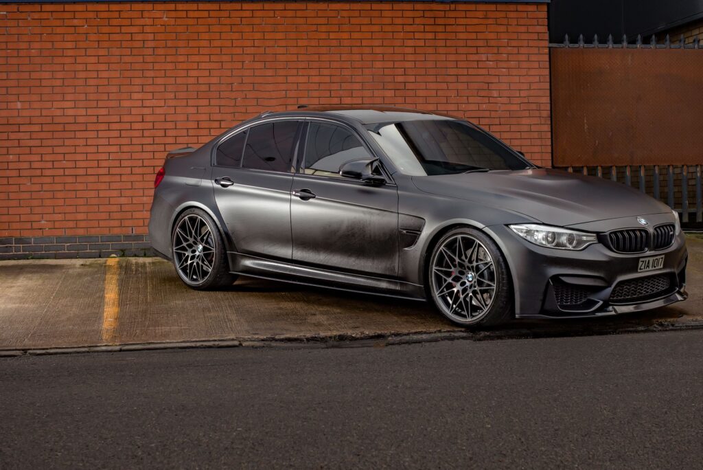 Stylish matt black BMW M3 parked outdoors against a classic brick wall in Birmingham.