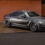 Stylish matt black BMW M3 parked outdoors against a classic brick wall in Birmingham.