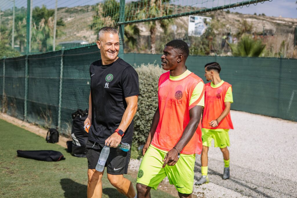 Coach and players enjoying sunny outdoor football training session.