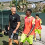 Coach and players enjoying sunny outdoor football training session.