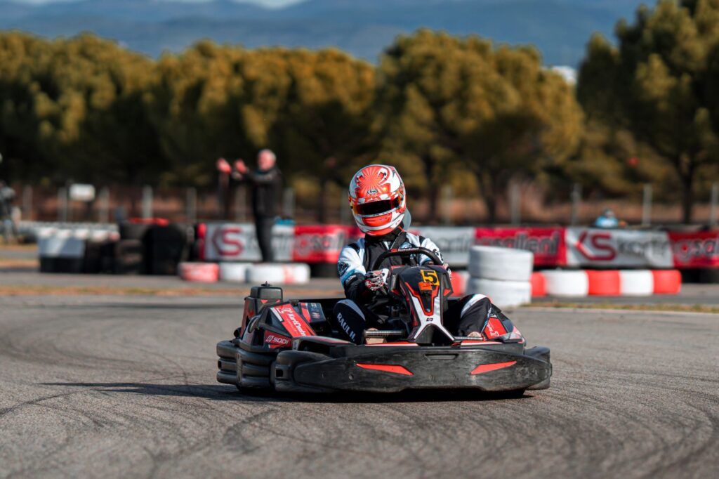 A person drives a go-kart on an outdoor racing track surrounded by trees.