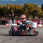 A person drives a go-kart on an outdoor racing track surrounded by trees.