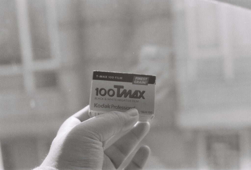 Close-up of Kodak T-Max 100 black and white film held by a hand, showcasing vintage photography equipment.