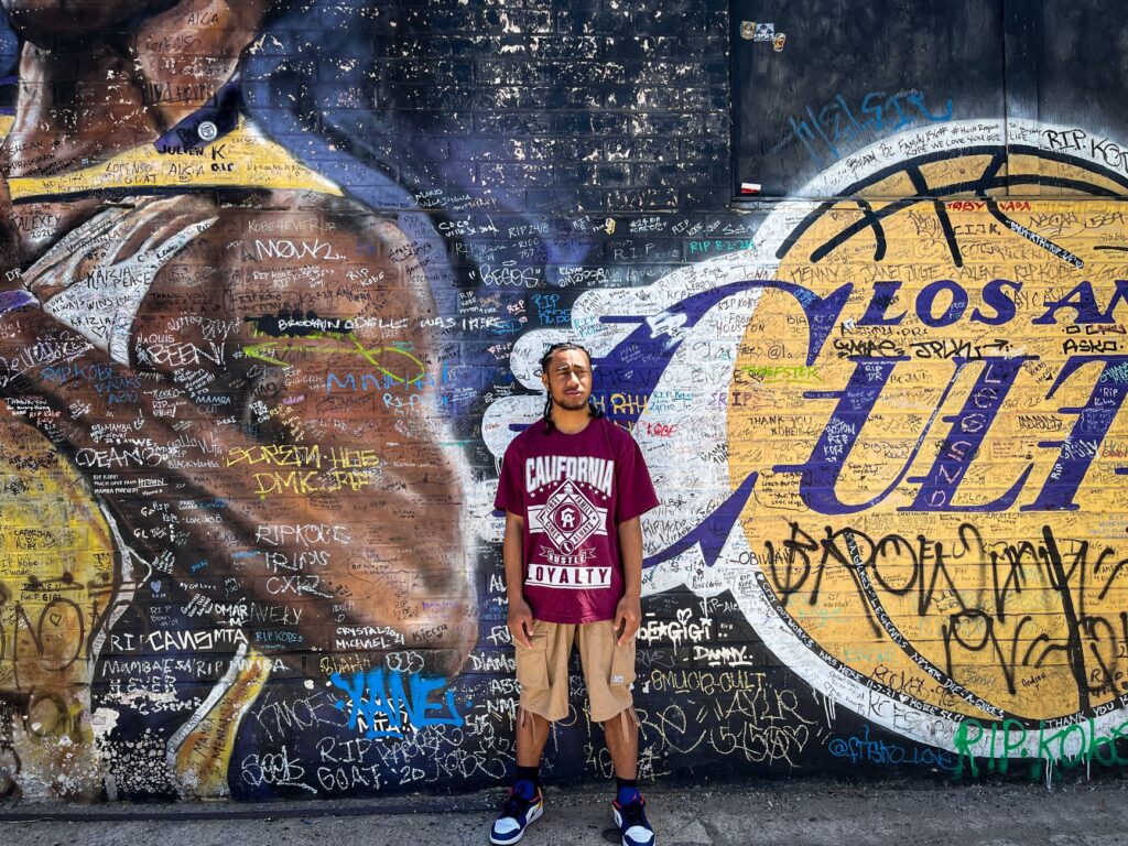 Man stands in front of colorful Los Angeles mural, vibrant street art scene.