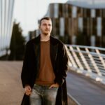 Young man in fashion coat walking on a modern bridge in Manchester, capturing urban style.