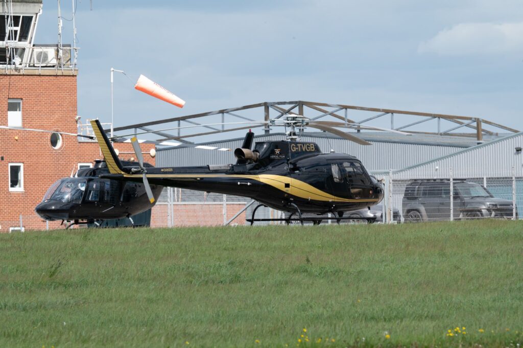 A black and gold helicopter parked at an airport with a control tower.