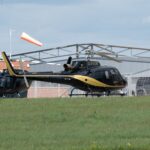 A black and gold helicopter parked at an airport with a control tower.