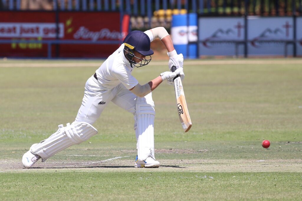 Action shot of a cricket player batting on the field during a sunny day match.