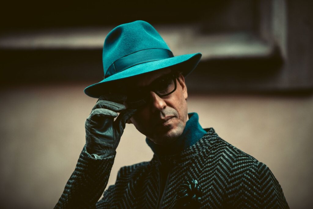 Close-up of a fashionable man in Milan wearing a teal hat and sunglasses.