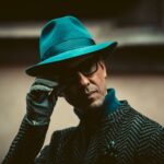 Close-up of a fashionable man in Milan wearing a teal hat and sunglasses.