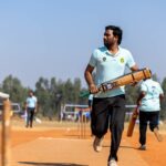 Cricketer with bat ready on sunny day outdoor field, sporting event.