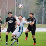 Players engage fiercely during a soccer match on a lush green field outdoors.