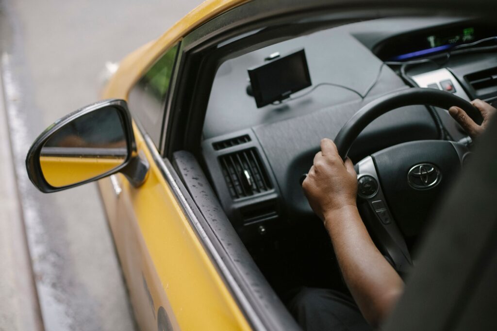 From above of crop unrecognizable person driving modern yellow taxi car with GPS navigator on city street in daytime