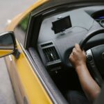 From above of crop unrecognizable person driving modern yellow taxi car with GPS navigator on city street in daytime