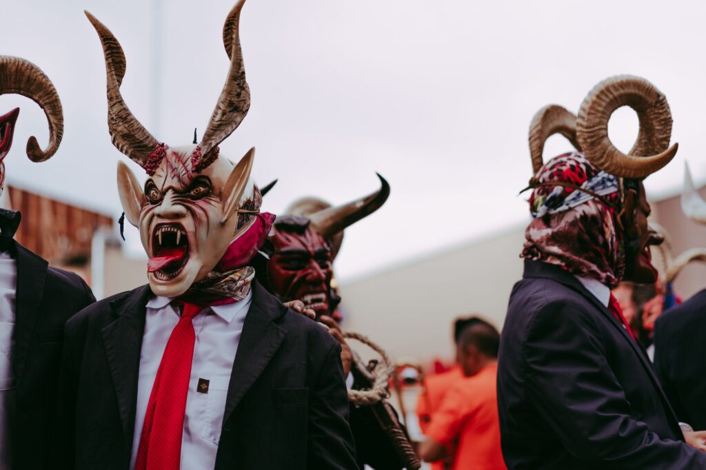 Men in elaborate devil masks perform a traditional folk dance outdoors.