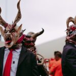 Men in elaborate devil masks perform a traditional folk dance outdoors.