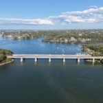 Aerial view of Captain Cook Bridge spanning over Georges River, connecting lush landscapes under a clear blue sky.