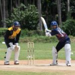 Cricketer ready to bat with wicketkeeper in sports gear outdoors.