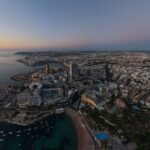 Discover a breathtaking aerial view of St. Julian’s, Malta as the sun sets, illuminating the coastline and cityscape.