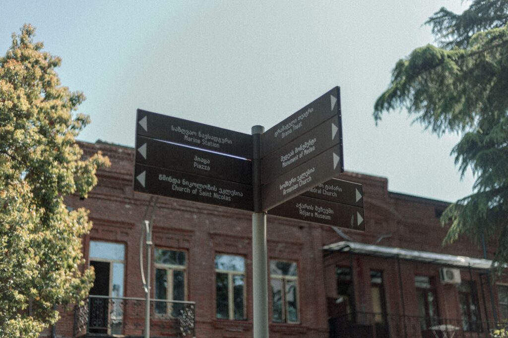 Signpost with directions to landmarks in Batumi, Georgia, with trees and buildings in view.