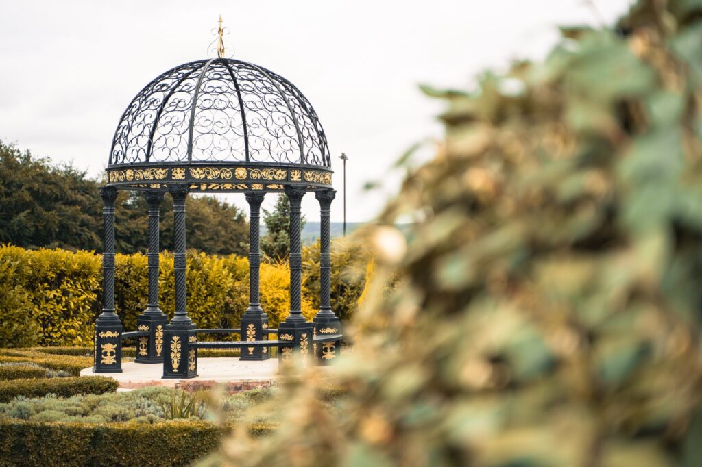 Charming garden gazebo with ornate wrought iron structure surrounded by lush greenery in Papplewick, England.