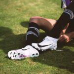 Close-up of a soccer player tying cleats on a sunny grass field, ready for action.