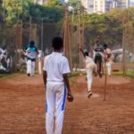 Young cricketers practice their skills on a dusty pitch in a Mumbai playground, showcasing local sports culture.