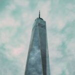 Dramatic view of One World Trade Center in New York City against overcast skies.