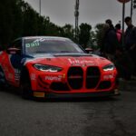 A sleek BMW M4 racecar on city streets during a motorsport event in Monza, Italy.