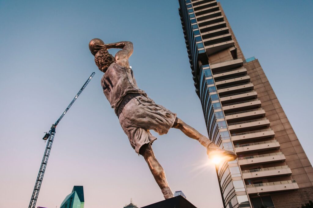Dramatic statue of a basketball player with skyscrapers and blue sky backdrop.