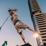 Dramatic statue of a basketball player with skyscrapers and blue sky backdrop.