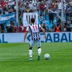 Soccer player number 11 in action on field during a match with cheering fans in the background.
