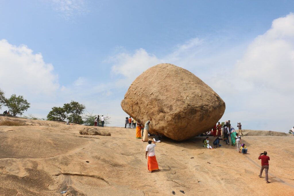 Tourists gather around the iconic Krishna's Butter Ball in Mahabalipuram, India, a popular travel attraction.