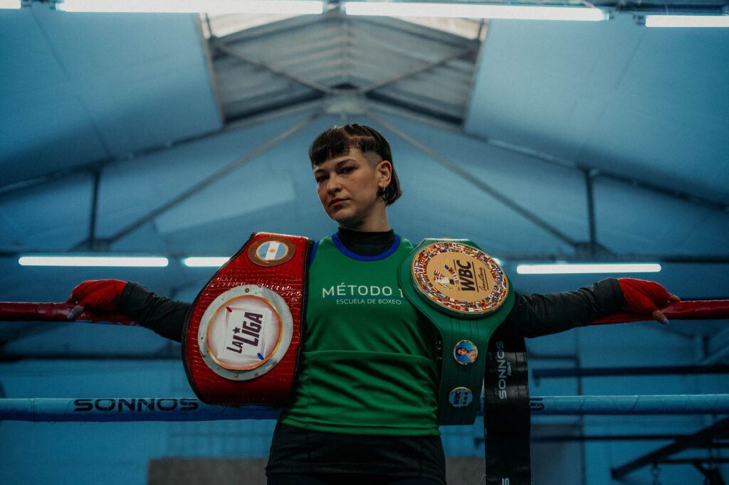 Female boxer in Buenos Aires gym displaying championship belts, showcasing strength and determination.