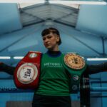 Female boxer in Buenos Aires gym displaying championship belts, showcasing strength and determination.