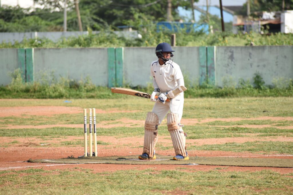 A cricketer in action on a sunny outdoor field in full gear, ready to bat.